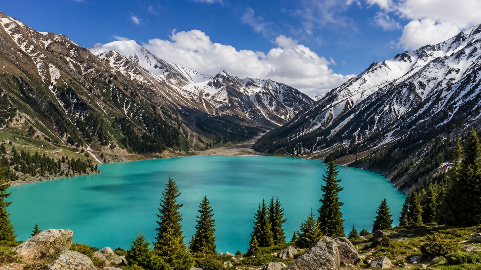 Panoramic view of Big Almaty Lake with turquoise water, pine slopes and snow-capped mountains near Almaty, Kazakhstan