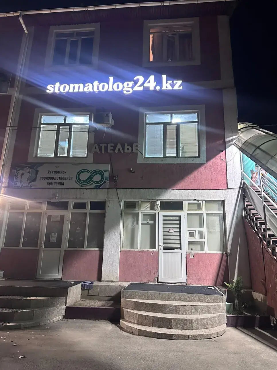 Филиал кіреберісінің үстінде түнде жарқырап тұрған stomatolog24.kz маңдайшасы
