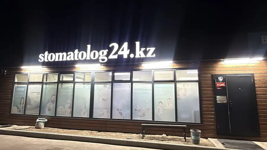 Филиал терезелерінің үстінде түнде жарқырап тұрған stomatolog24.kz маңдайшасы