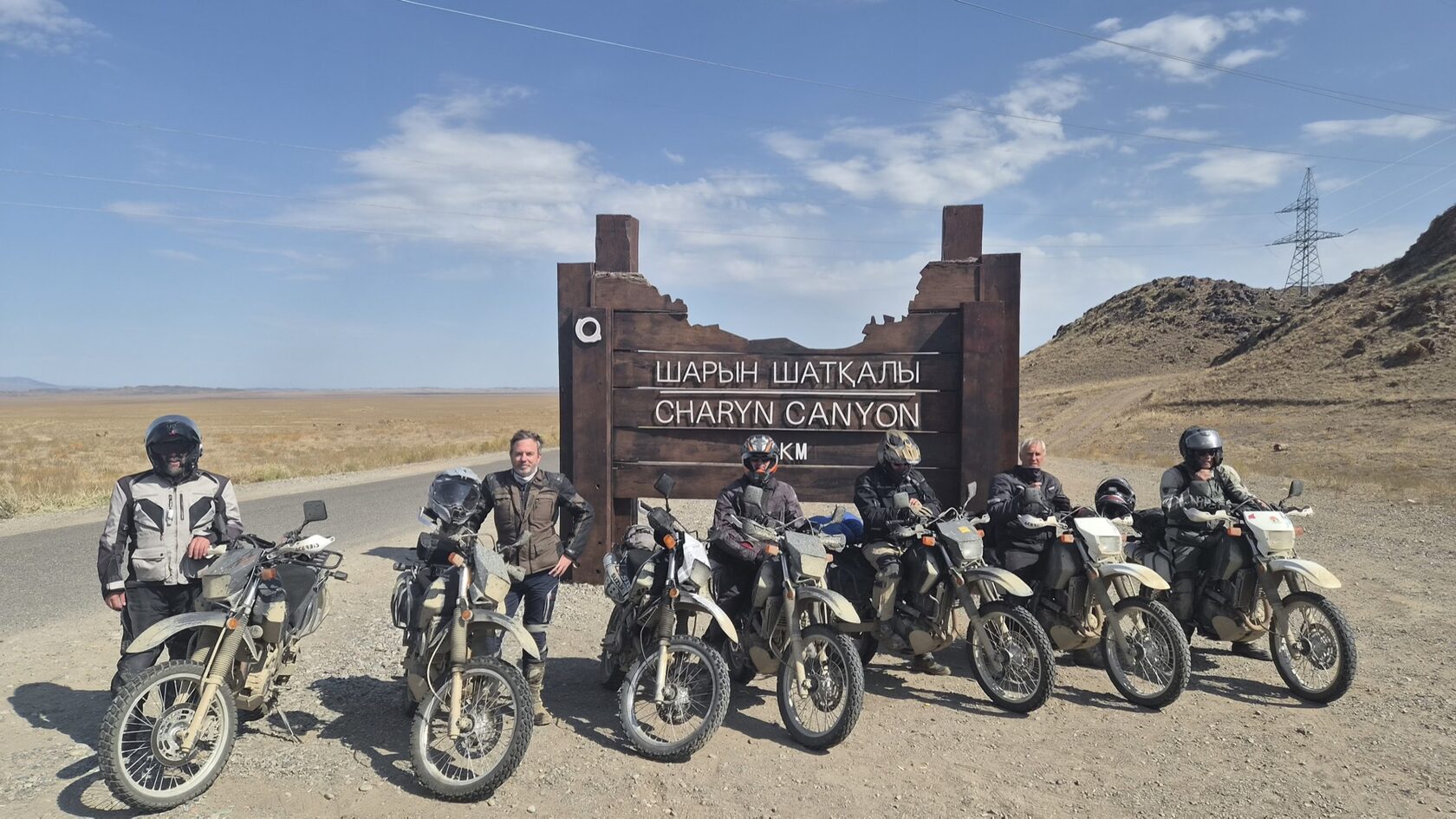 SilkOffRoad riders on Suzuki DR650SE motorcycles at the Charyn Canyon sign