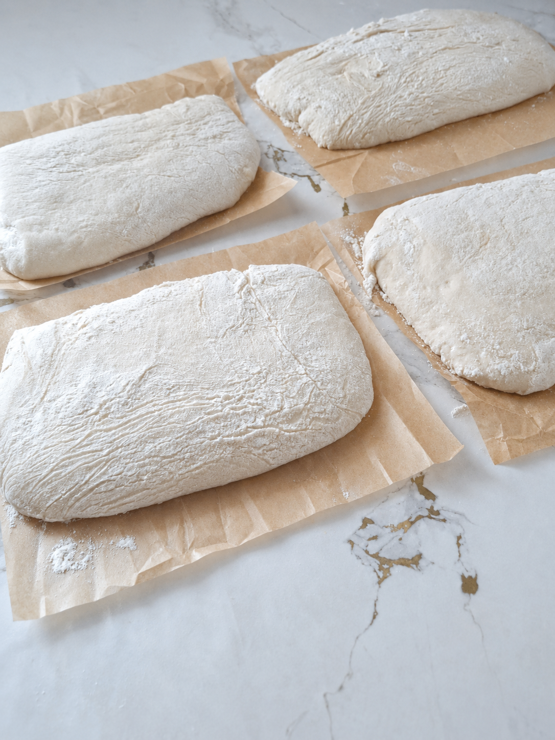 Four ciabatta dough pieces during final proofing on parchment paper